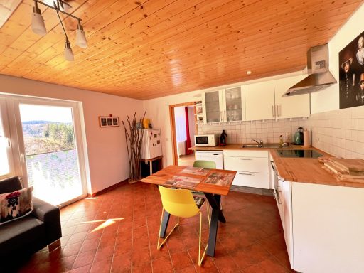 Helle Küchenzeile mit Esstisch, Stühlen und Zugang zum Balkon. Holzdecke und moderne Ausstattung.