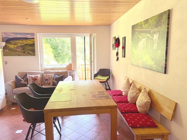 Heller Raum mit Esstisch, Sitzbank, Stühlen und Kunstwerken an der Wand.